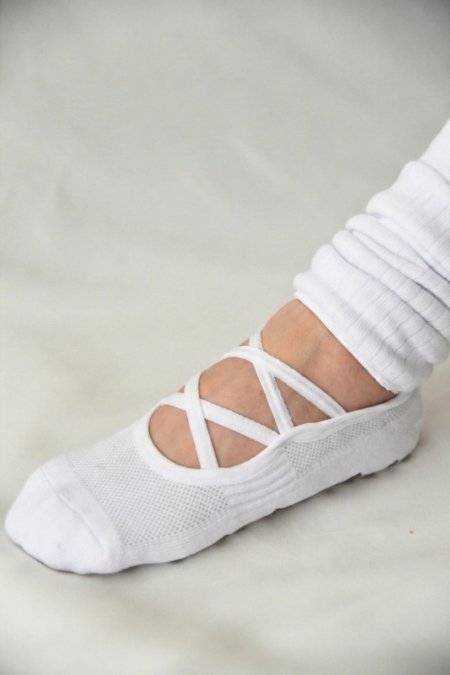 White ballet shoe with criss-cross straps on a neutral background